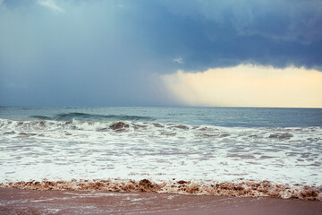 Ocean waves rolling onto sandy beach with storm clouds on horizon