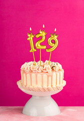 Pink birthday celebration cake with number 129 candle