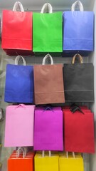 A colorful display of paper shopping bags with sturdy handles hanging on a store wall, neatly arranged in various bright shades for packaging and gift purposes