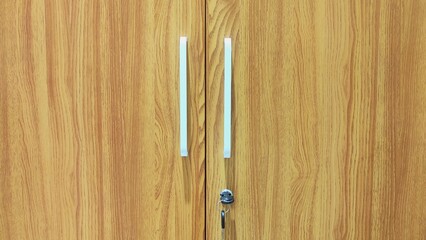 Close-up of wooden wardrobe doors with vertical grain pattern, white minimalist handles, and a secure lock and key attached for storage safety.