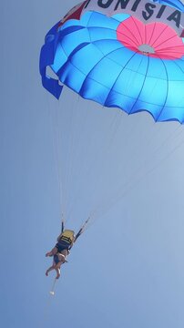 Adventurous couple tandem parasailing over a bright blue sky during summer vacation, vertical video