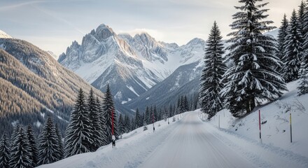 Fototapeta premium Snowy mountain road winding through a winter landscape with towering peaks and evergreen trees