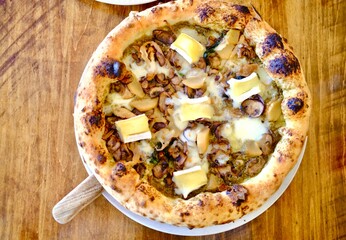 A freshly baked pizza with a golden crust, topped with mushrooms and chunks of creamy cheese, served on a rustic wooden table