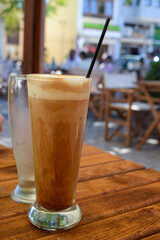 Refreshing Greek Frappé coffee at an outdoor cafe in Greece. Cold Greek iced coffee drink made with instant coffee and milk, served in a glass with a straw.