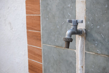 A closed outdoor tap with a hosepipe attachment. Garden tap outside on a tiled garden wall.
