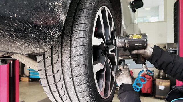 Mechanic Using a Tool to Remove Screws from a Car Tire at Service Center