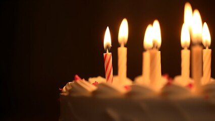 Close-up of a birthday cake with lit candles, glowing warmly in soft diffused light.