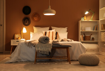 Interior of bedroom with plaids on soft bench and glowing lamps at night