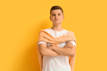Obraz premium Confident young boy with folded arms and casual style on bright yellow background, youthful expression and modern fashion
