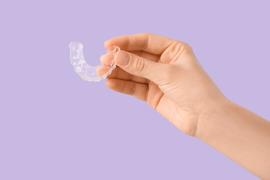 Female hand with occlusal splint on lilac background