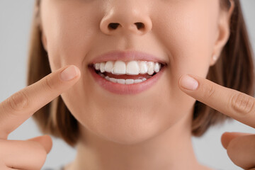 Obraz premium Young woman pointing at her teeth with occlusal splint on light background, closeup