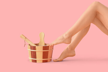 Legs of woman with water bucket for sauna on pink background © Pixel-Shot
