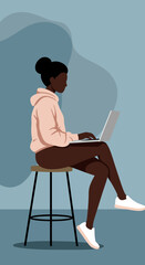Young Black woman focused on her laptop, sitting casually on a stool. Represents remote work, online learning, freelancing, and modern productivity.