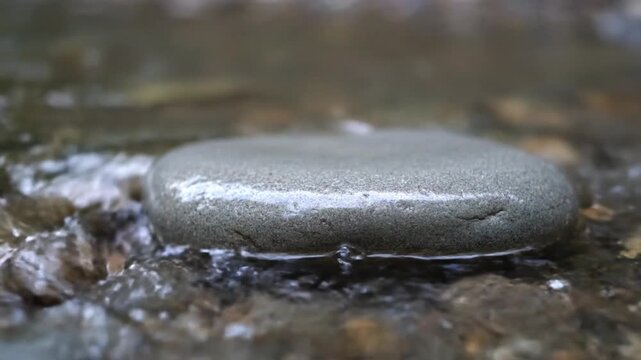 Close-up of clear water gently flowing over a smooth flat grey river stone Tranquil nature scene with peaceful ripples and subtle movement perfect for meditatio