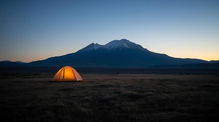 Illuminated Tent on Grassy Plain at Dusk with Mountain Range