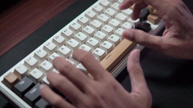 Close-up hands typing on a mechanical keyboard with white keycaps and gold details on a wooden desk.
