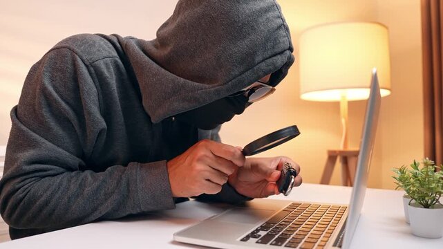 The hacker&rsquo;s use of a magnifying glass on a lock illustrates the search for system weaknesses, highlighting cybersecurity risks, hacking methods, encryption, and data protection challenges.
