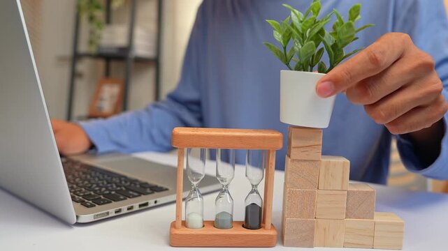 Working on a laptop while building a staircase of blocks to support a plant highlights upward growth, strategic planning, resilience, learning, and the nurturing of both career and personal ambitions.