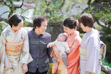 A group of women are standing together, one of them holding a baby. Scene is warm and friendly, as the women are smiling and enjoying each other's company