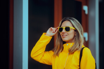 Woman Wearing Yellow Sunglasses and Raincoat feeling Positive. Carefree person feeling happy about the weather changing during autumn season
