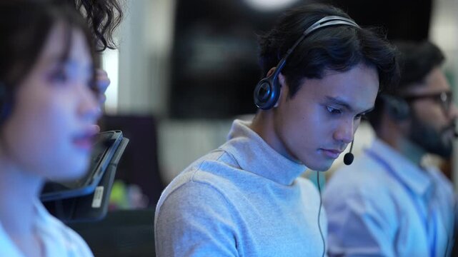 A friendly team of operators with headsets smiles while talking to customers. The diverse group works in a busy call center, helping people and providing good service