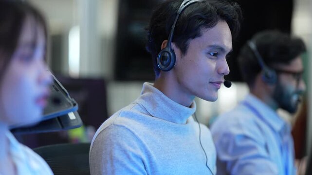 A friendly team of operators with headsets smiles while talking to customers. The diverse group works in a busy call center, helping people and providing good service