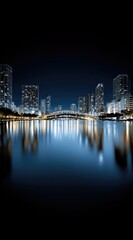 Obraz premium Illuminated city skyline reflected in tranquil waters at night. Tall buildings with bright windows under a dark sky with a bridge connecting structures