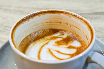 Extreme close up view of a half cafe latte on the wooden table. grey or gray cup, mug. ceramic. art. copy space, empty, free, negative, text, design. brown. white. after drink, drank. coffee.