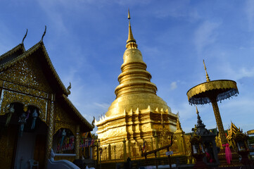 Naklejka premium Church and Golden pagoda in evening, Lanna Architecture, Symbols of Buddhism, South East Asia at wat phra that hariphunchai in Lamphun, north, Thailand