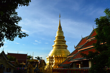Naklejka premium Church and Golden pagoda in evening, Lanna Architecture, Symbols of Buddhism, South East Asia at wat phra that hariphunchai in Lamphun, north, Thailand