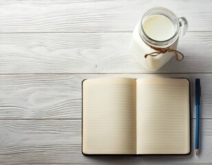 Open notebook and jar of milk on white wooden table 
