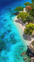 Aerial view of a secluded beach. Turquoise water meets a sandy shore lined with trees. Autumn hues add a touch of color. Rocky cliffs frame the scene