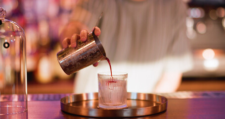Pouring cocktail. Cold aperitif. Male barman adding red liquid from metal shaker to glass. Making big ice cube negroni on pub counter.