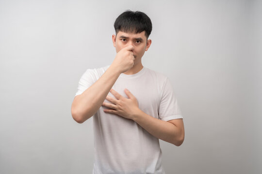 A young man with a disgusted expression pinches his nose, reacting to a foul smell or air pollution. Suitable for health, medical, environmental, and lifestyle concepts.