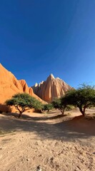 Sunny desert landscape with red rock formations and small trees against a bright blue sky, creating a vivid and contrasting scene