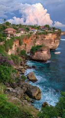 Coastal scene features high cliffs dotted with houses above turquoise water, waves crashing on rocks, and a dramatic, cloudy sky at dusk