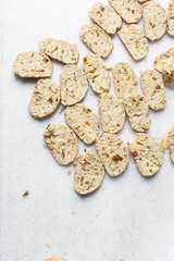 overhead view of slices of savory biscotti, top view of thinly sliced bread for making bread chips, top view of crostini bread slices on marble countertop
