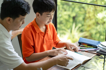 Asian father helps son to do her homework for the school.
child study together homeschooling concept getting homework help from father