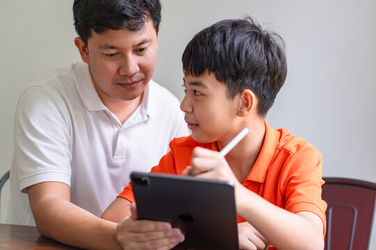 Asian father and son using tablet teaching son to draw
playing with digital tablet at desk fatherhood