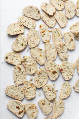 overhead view of slices of savory biscotti, top view of thinly sliced bread for making bread chips, top view of crostini bread slices on marble countertop