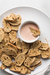 overhead view of slices of savory biscotti in dip, top view of thinly sliced bread chips in sauce, top view of crostini bread slices on marble countertop