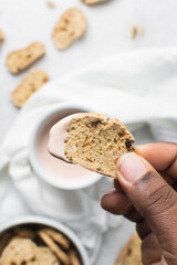 overhead view of slices of savory biscotti in dip, top view of thinly sliced bread chips in sauce, top view of crostini bread slices on marble countertop