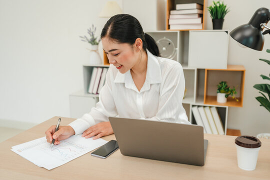 happy woman writing cocument or paperwork with laptop at home office