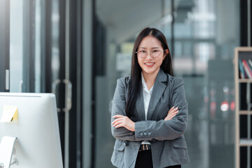 Portrait of a smiling asian businesswoman standing with arms crossed in a modern office, showcasing confidence and professionalism © amnaj