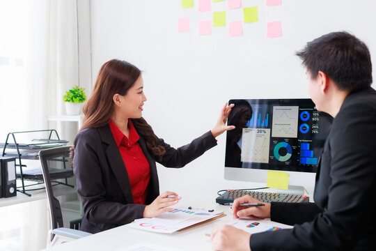 Asian business people working together discussing and analyzing financial charts and graphs using desktop computer in modern office