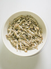 Dried anchovies in a white bowl on a white background.