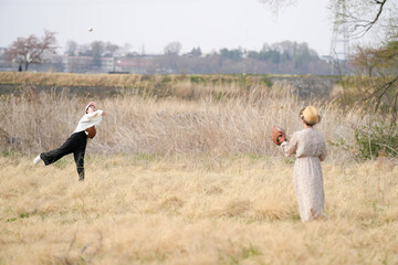 Two women playing baseball in a field. One is throwing the ball and the other is catching it