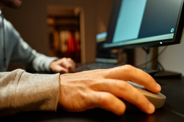 Close up of male hand holding computer mouse on desk near keyboard. Concept of office work and technology use