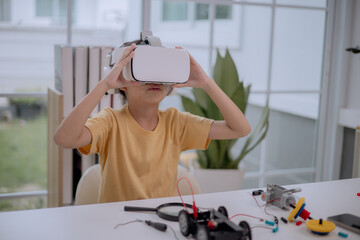 Asian girl using VR headset while working on robotics STEM project. Concept of child creativity, digital learning, virtual reality, innovation, future technology and immersive education for kids.