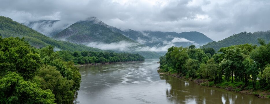 Misty mountains meet a river flowing through lush green forests